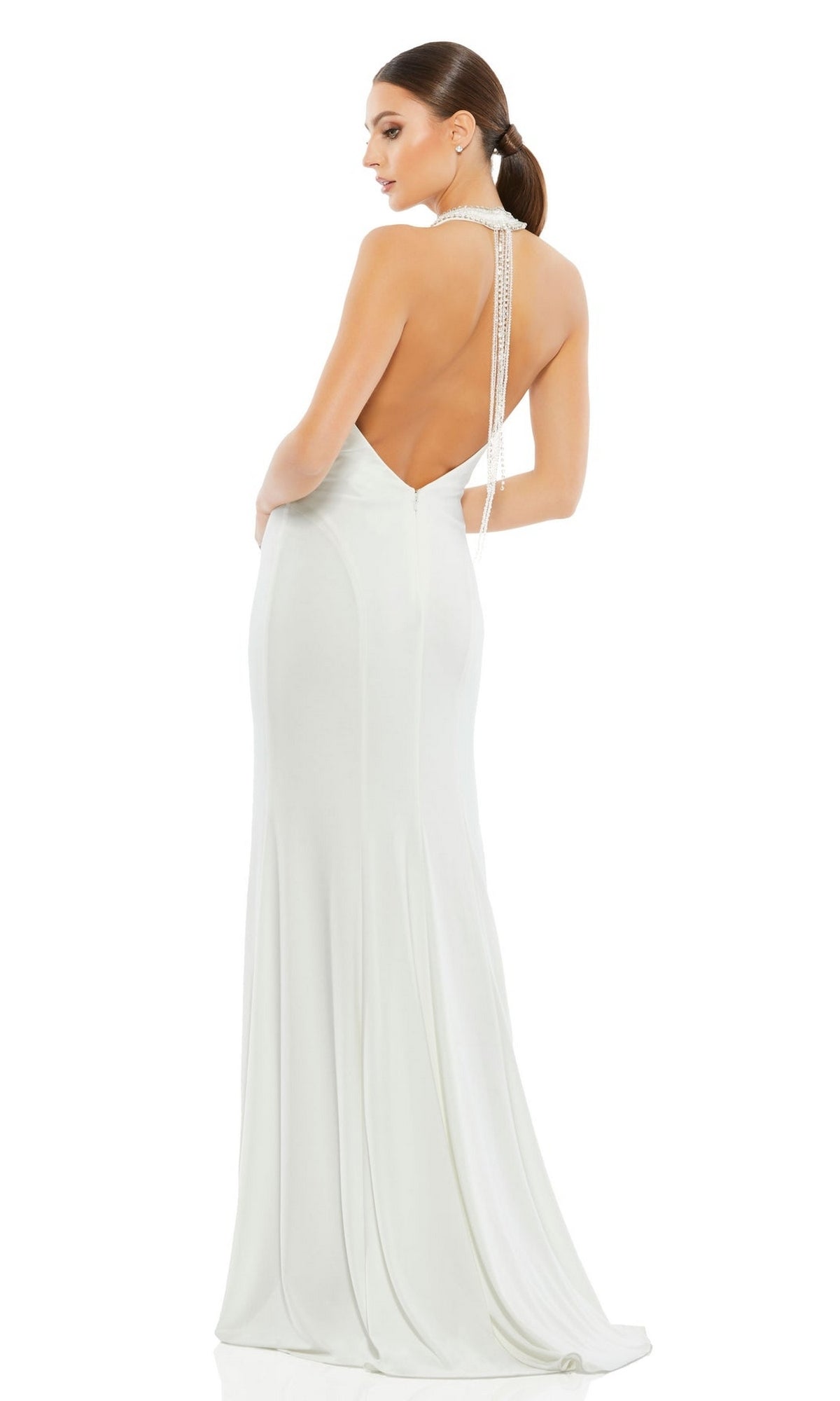 A woman stands against a white background wearing the Long Formal Dress 25572 by Mac Duggal—a floor-length white gown featuring an open back with a deep V and pearl-like straps.